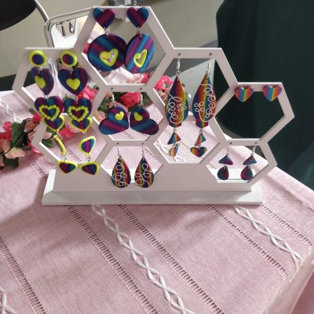A collection of handmade, polymer clay earrings displayed on a simple tessellated hexagon stand. 